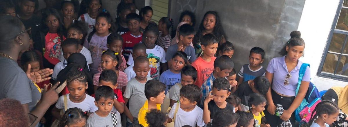 A large group of children excitedly waiting in line to receive school supplies during a back-to-school drive.